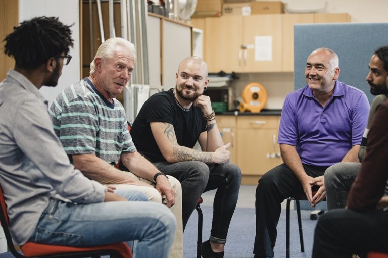 Diverse group of men are talking and laughing together in a mental health support group.